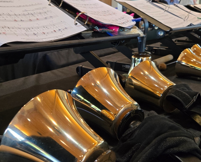 Close up of row of hand bells laying in front of sheet music on stands