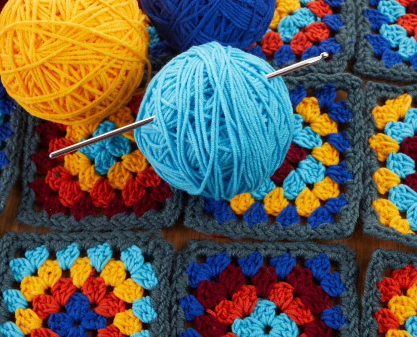 colorful crocheted squares on table with spools of blue and gold yarn