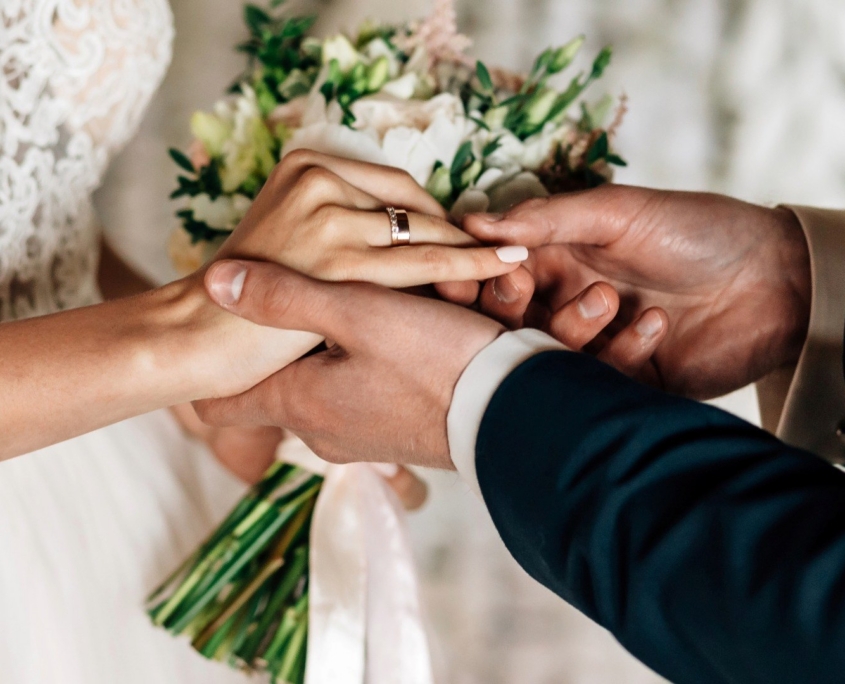Couple holding hands with rings and flower bouquet at wedding