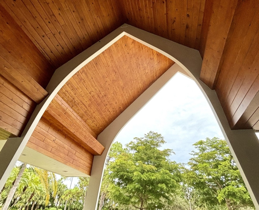 Exterior Chapel beams with wooden shiplap ceiling and treetops in the distance