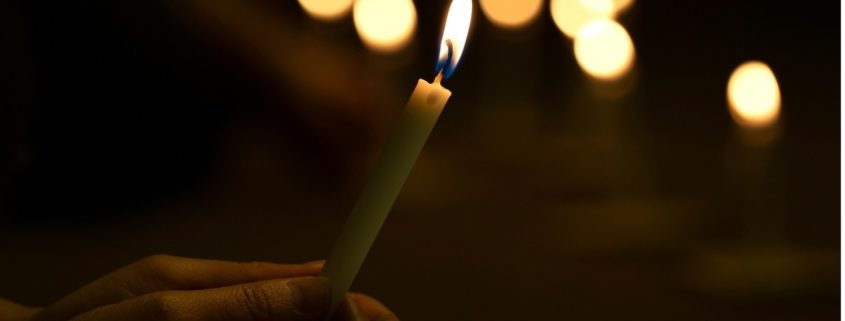 Hands holding single lit candle with dark background