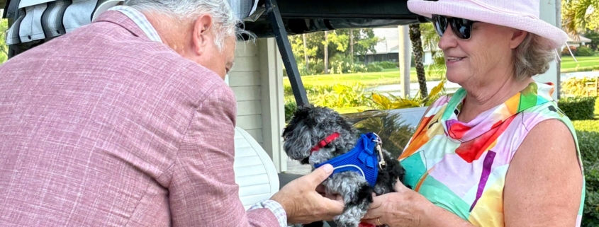Pastor Carr blessing small dog held by woman with golf cart behind her