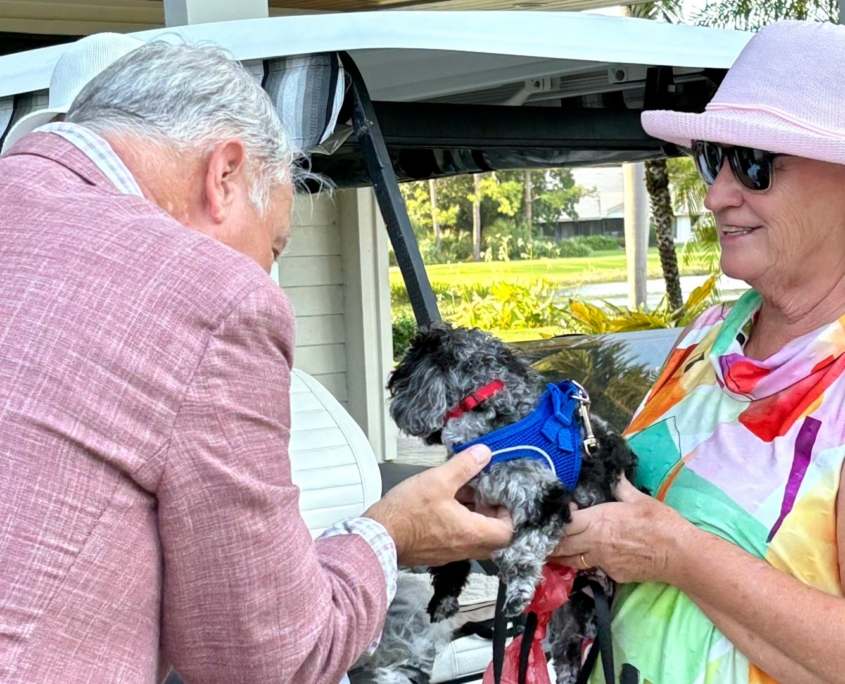 Pastor Carr blessing small dog held by woman with golf cart behind her