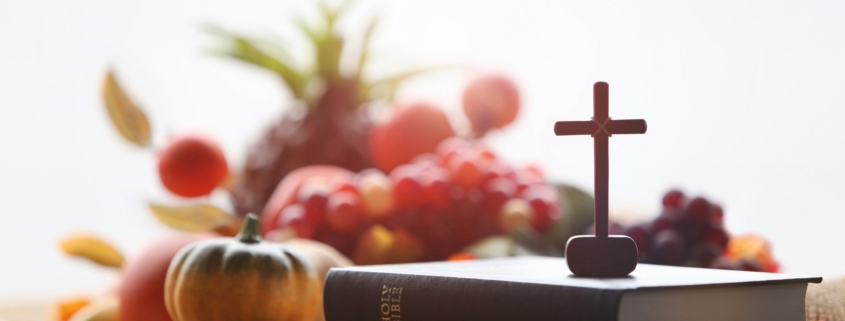 Wooden cross on brown bible with pumpkins, fruit and vegetables on a table