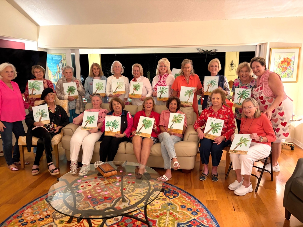 About 20 women sitting on sofa or standing behind it holding pictures of palm trees they drew
