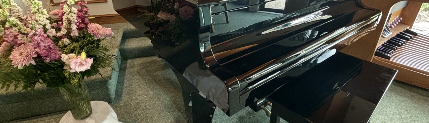 Black baby grand piano with organ in background at chapel