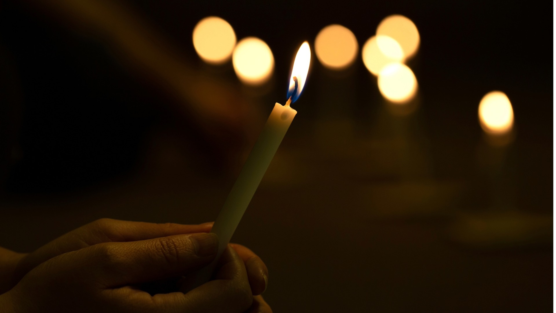 Hands holding single lit candle with dark background