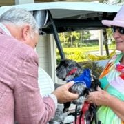 Pastor Carr blessing small dog held by woman with golf cart behind her