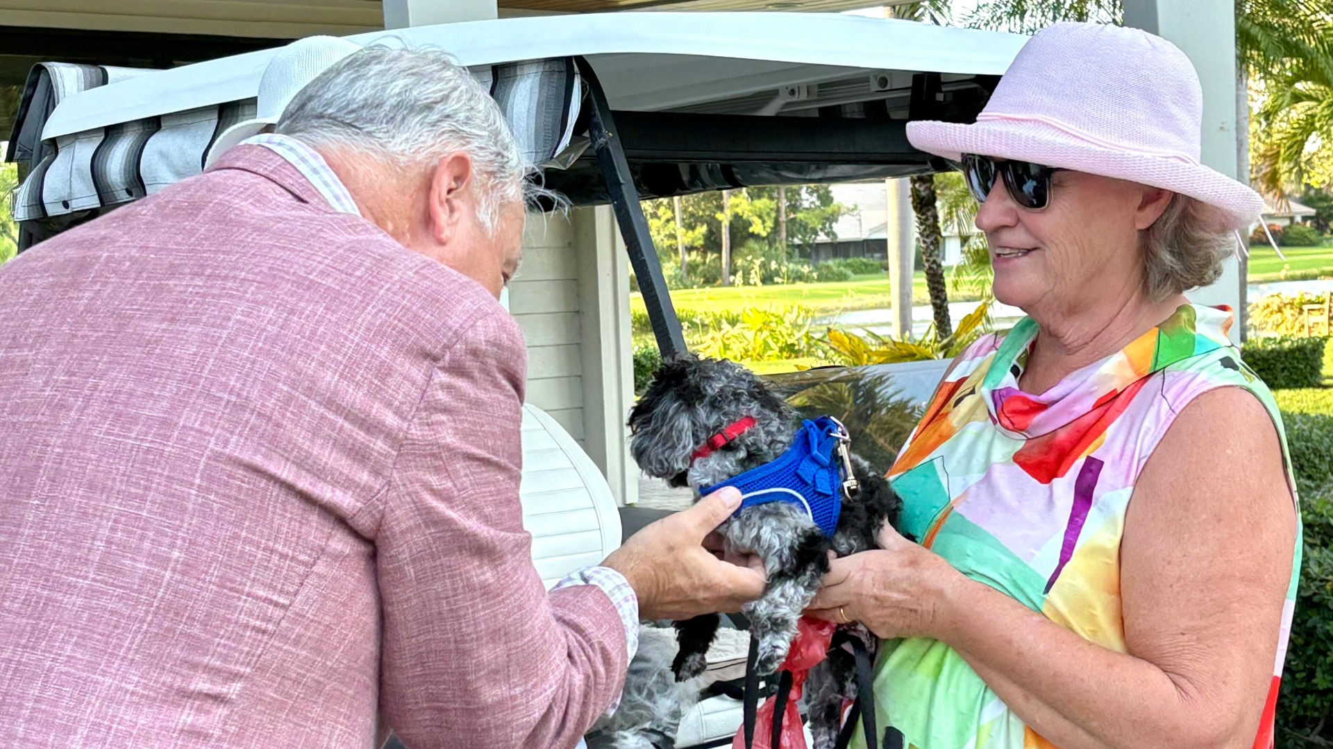 Pastor Carr blessing small dog held by woman with golf cart behind her
