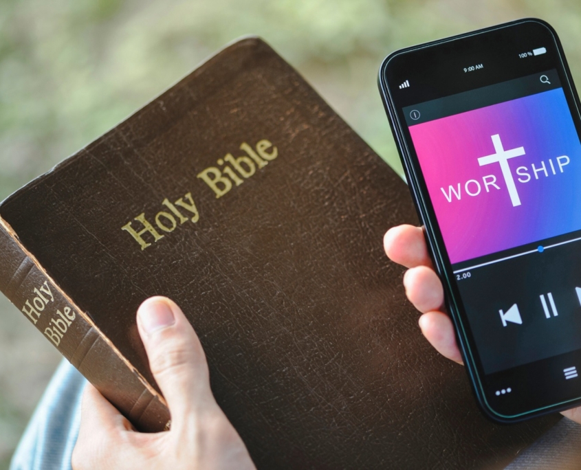 man's hands holding bible and cell phone
